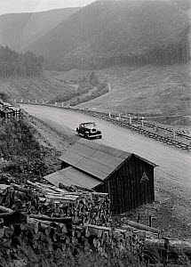 10547073
&copy; NMPFT - Zoltan Glass
Car on mountainous road with shed and timber in foreground. Photographed by Zoltan Glass, c.1930.