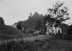 10547080
&copy; NMPFT - Zoltan Glass
Car on road with timber framed houses and ruins in background. Photographed by Zoltan Glass, c.1930.