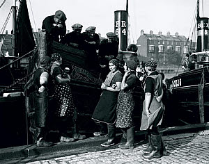 10316022
&copy; NMeM Daily Herald Archive
Fishergirls talking to fishermen, Great Yarmouth, Norfolk, 8 October 1935.